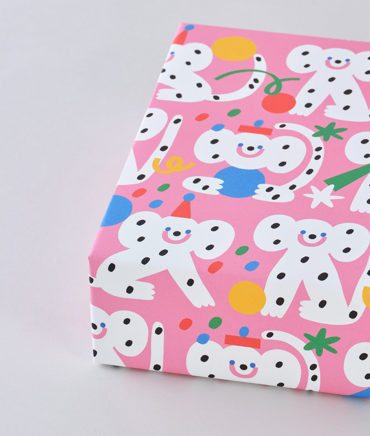 corner view of a present wrapped in polka dot monkeys celebrating with hats and streamers cover this pink celebration birthday wrapping paper