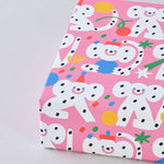 corner view of a present wrapped in polka dot monkeys celebrating with hats and streamers cover this pink celebration birthday wrapping paper