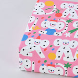 corner view of a present wrapped in polka dot monkeys celebrating with hats and streamers cover this pink celebration birthday wrapping paper