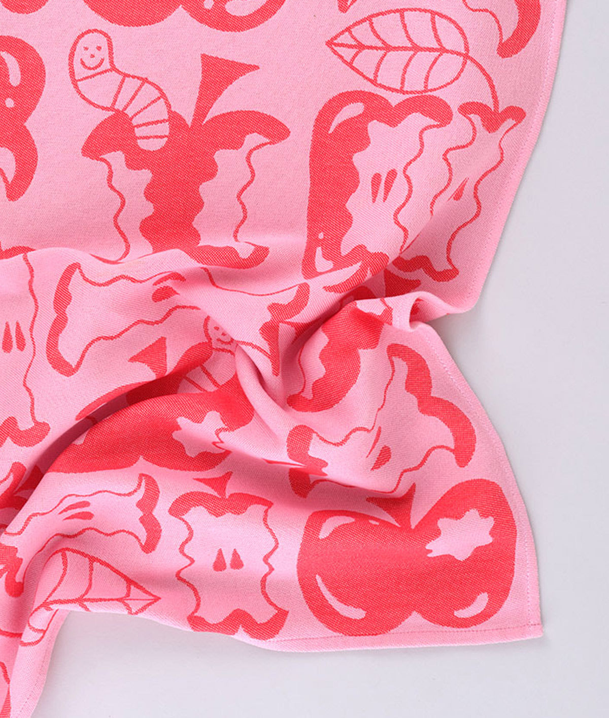 Corner detail of the pink apple a day tea towel featuring half eaten apples and cartoon worms