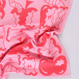 Corner detail of the pink apple a day tea towel featuring half eaten apples and cartoon worms