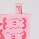 label detail of the pink apple a day tea towel. the pink label is a cartoon worm