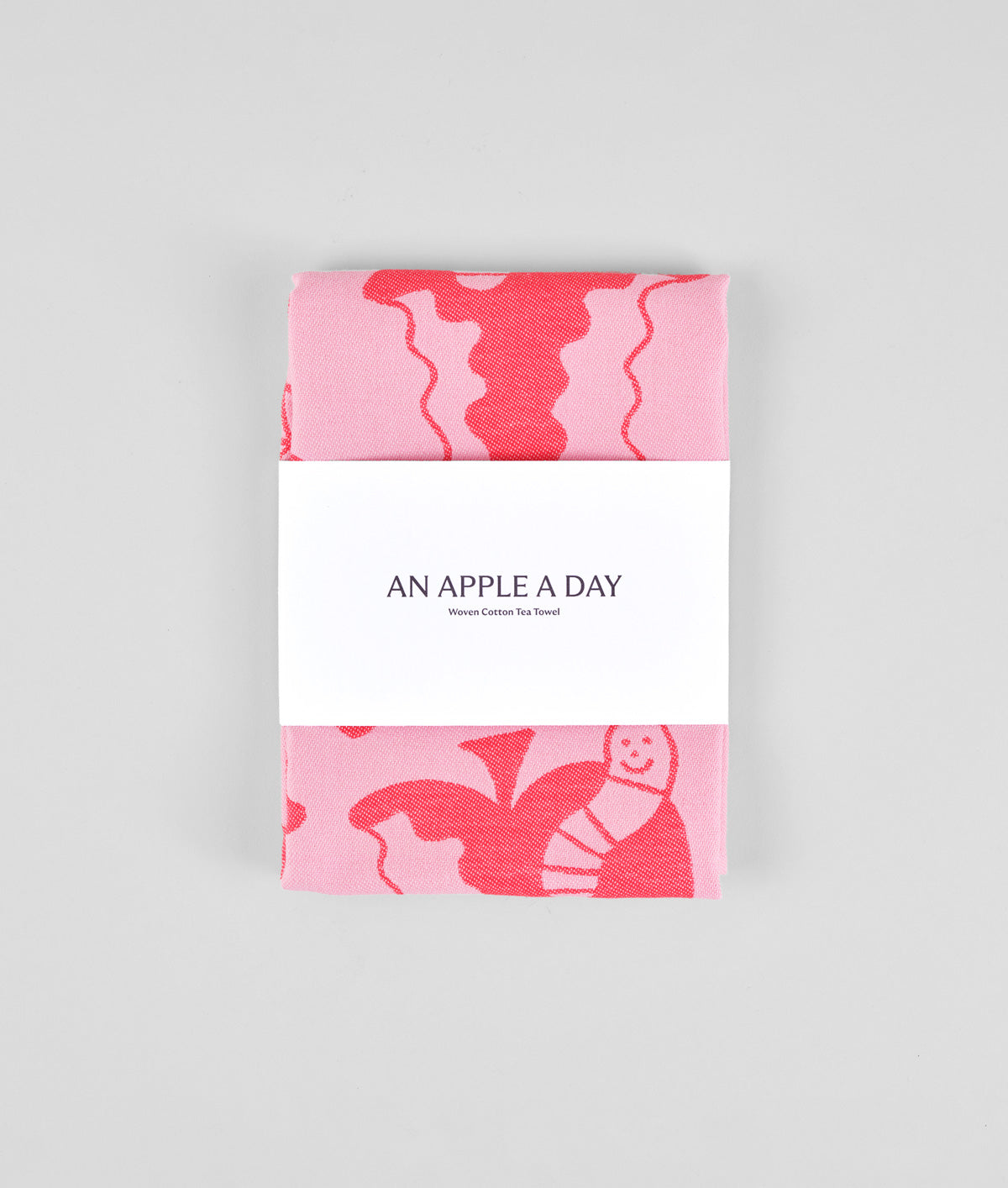 packaging detail of the pink apple a day tea towel featuring half eaten apples and cartoon worms