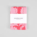 packaging detail of the pink apple a day tea towel featuring half eaten apples and cartoon worms