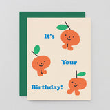 three sweet little oranges celebrating a birthday on a cream background with blue writing that reads it's your birthday!