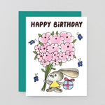Birthday card with a cartoon bunny holding pink flowers and a gift, on a light gray background.