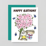 Birthday card with a cartoon bunny holding pink flowers and a gift, on a light gray background.