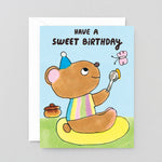 Birthday card with a cartoon bear holding a spoon and butterfly, text 'Have a sweet birthday' on a light blue background.