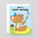 Birthday card with a cartoon bear holding a spoon and butterfly, text 'Have a sweet birthday' on a light blue background.