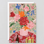 a bouquet of flowers and present on a greetings card and envelope against a grey background